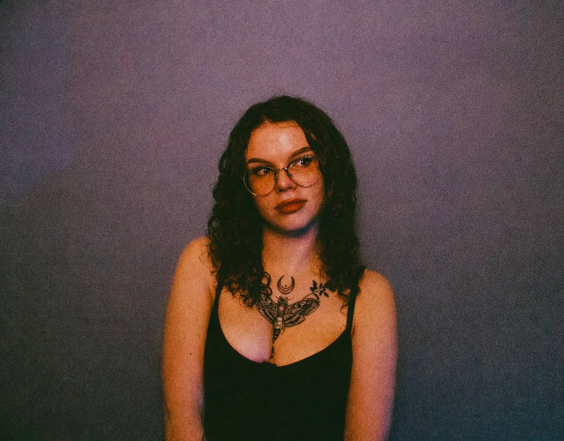 Booba, tattoo artist, photographed against a purple wall